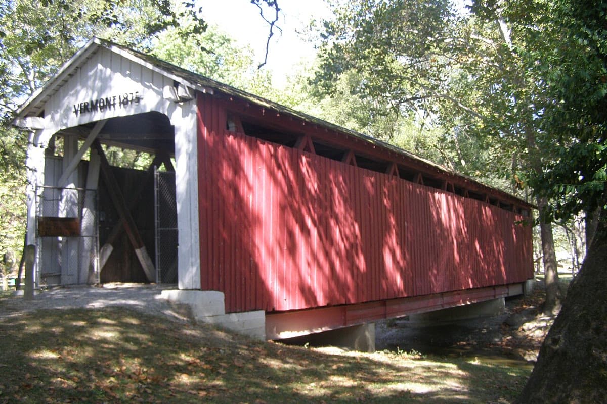 A red and white Vermont covered bridge from 1875 surrounded by trees