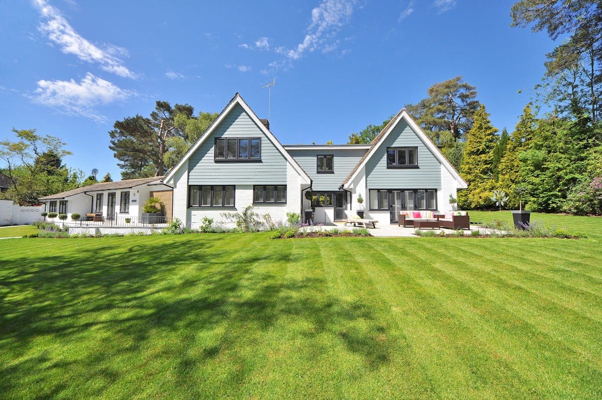A large white New England home with gabled roof and manicured lawn surrounded by trees