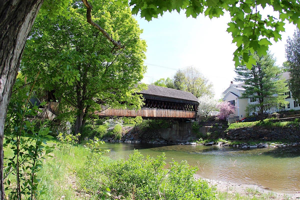 The Middle Covered Bridge in Woodstock, Vermont, spanning the Ottauquechee River surrounded by lush green foliage