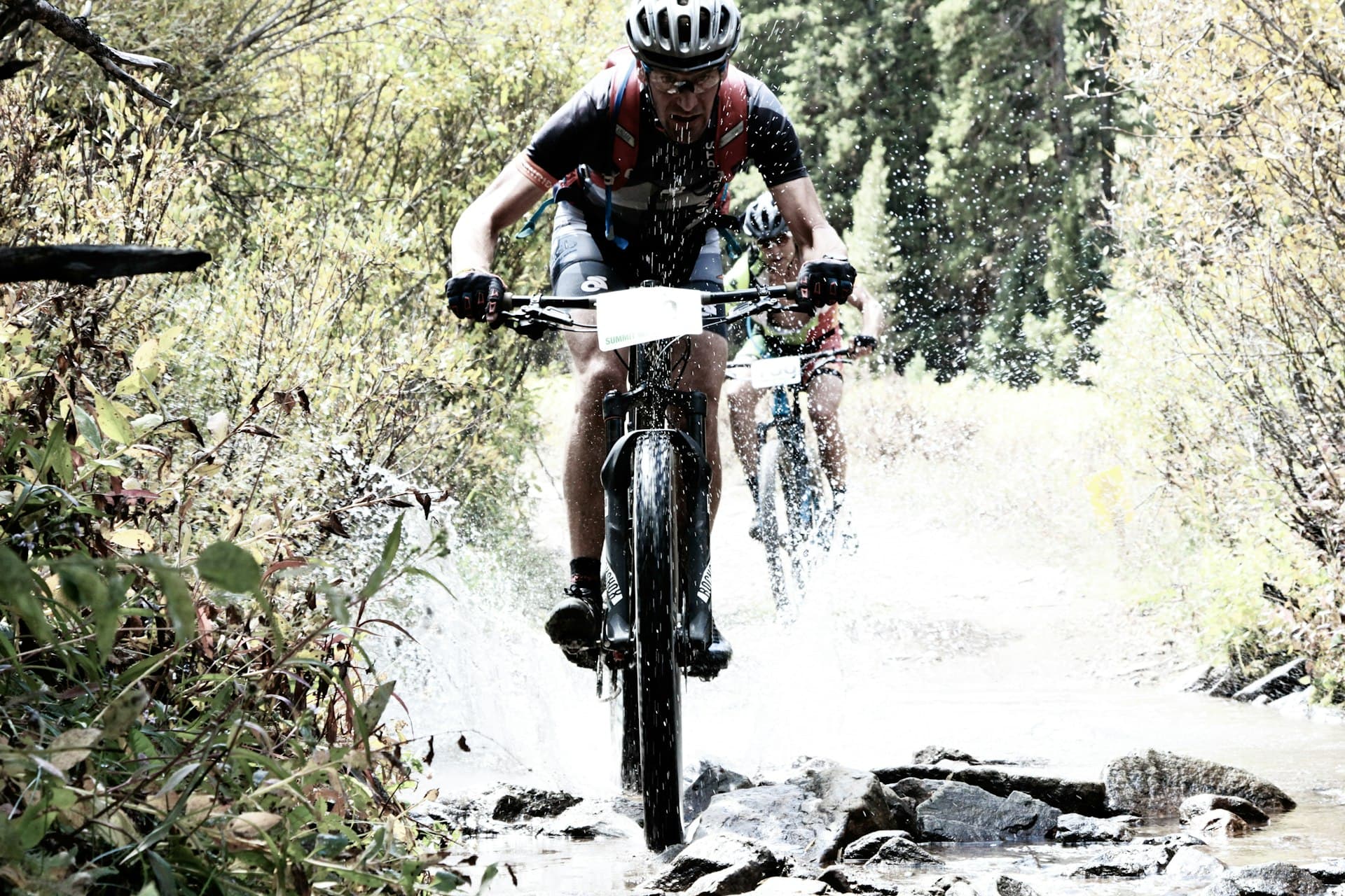Mountain bikers racing through creek on forest trail near Killington